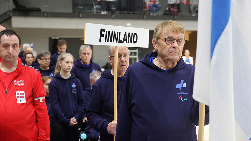 Suomen joukkue Finland -kyltin ja Suomen lipun kanssa avajaistilaisuudessa.