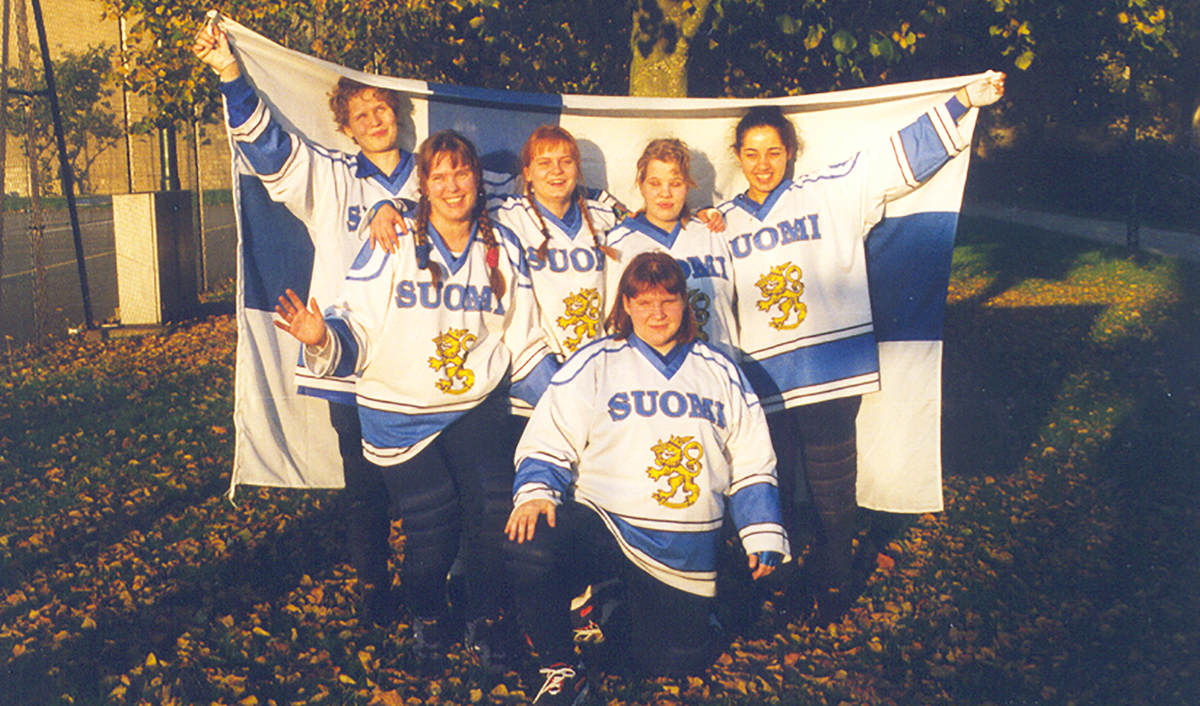 Naiset yhteiskuvassa Suomi-paidoissa ja ison Suomen lipun kanssa.