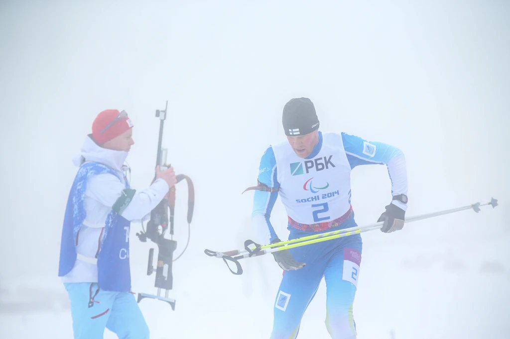 Jari Härkönen saapumassa ampumispisteelle, avustaja ojentamassa asetta.