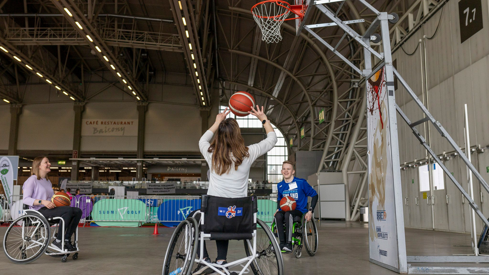 Iloiset nuoret pelaamassa pyörätuolikoripalloa.