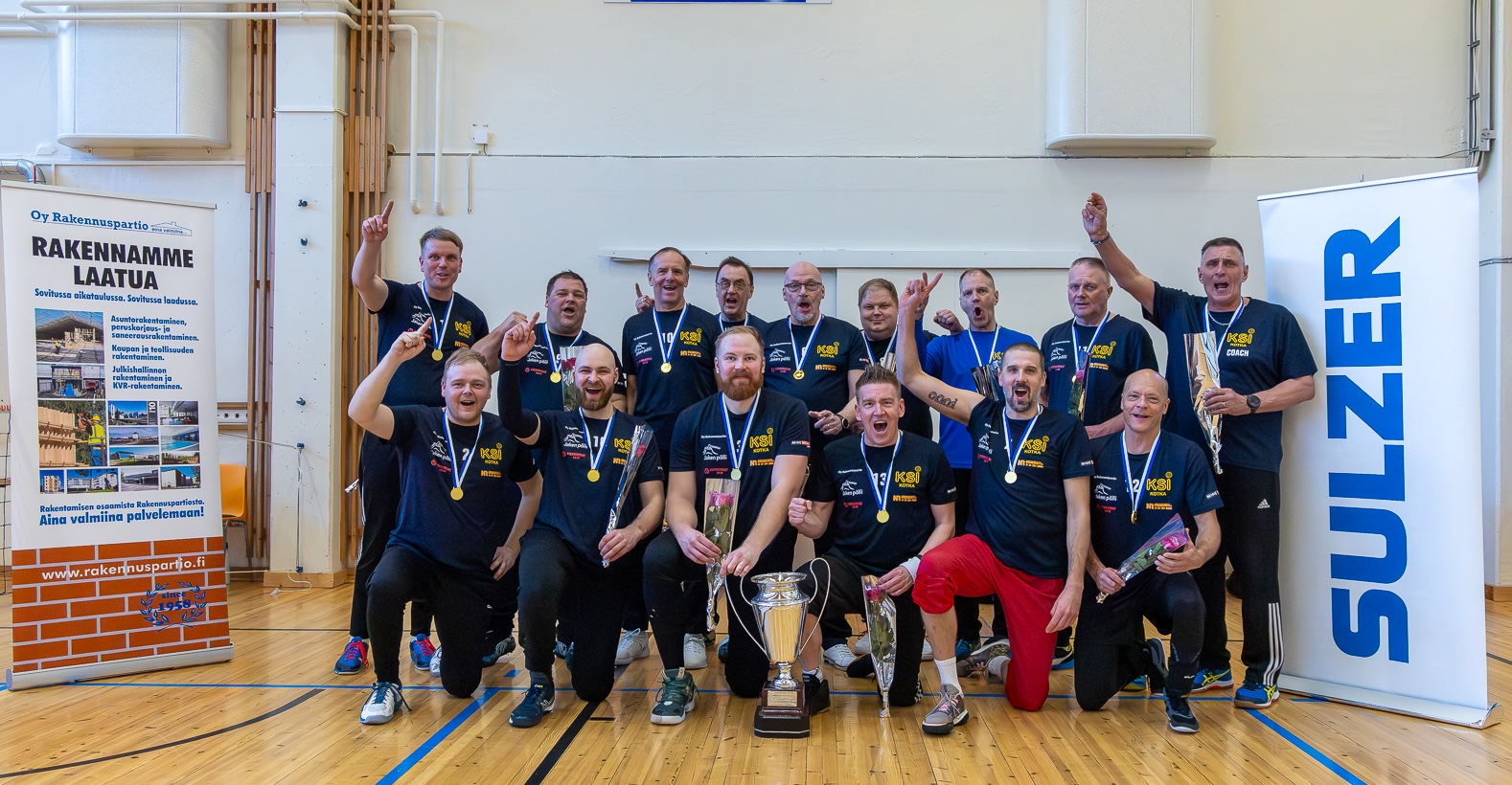Miesten mestarit poseeraamassa kameralle mitalit kaulassaan, ison pokalin kanssa.