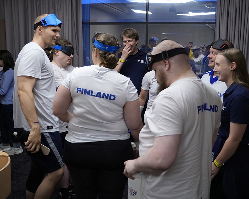 Pelaajia nauramassa valmentajien kanssa valkoisissa Finland-paidoissaan.