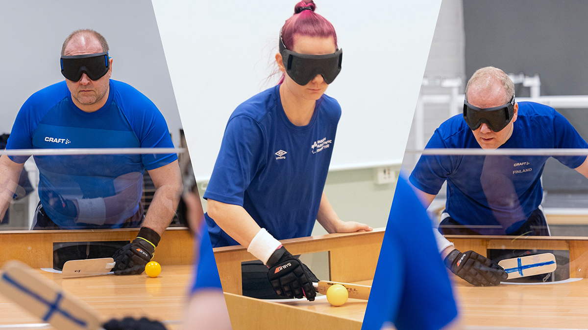 Pelaajat pelipöytiensä päädyssä lyömässä tai odottamassa palloa Suomen tummansinisissä maajoukkuepaidoissa, läpinäkymättömät pelilasit silmillään.