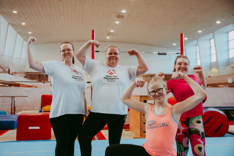 Iloisia Special Olympics -voimistelijoita näyttämässä hauiksia kameralle voimistelusalissa.