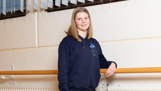 Venla Salo poseeraa hymyillen Paralympiakomitean hupparissa liikuntasalin vaalealla seinustalla.