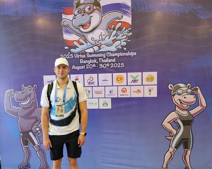 Nader Khalili kisapassi kaulassaan Virtus Swimming Championships 2025 -mainoslakanan edessä Thaimaassa.