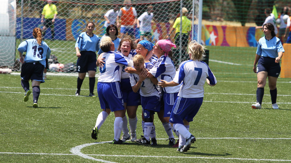 Iloisia Special Olympics -jalkapalloilijoita kentällä hurraamassa. Naisoletettuja.