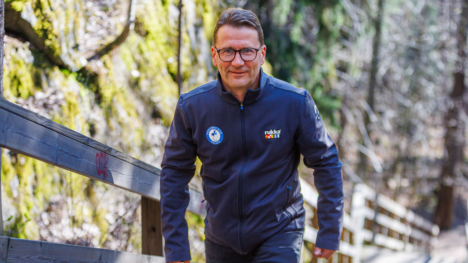 Olsa kipuamassa portaita luonnon siimeksessä paralympiajoukkueen kisatakki päällään, katsoen kameraan hyväntuulisena.