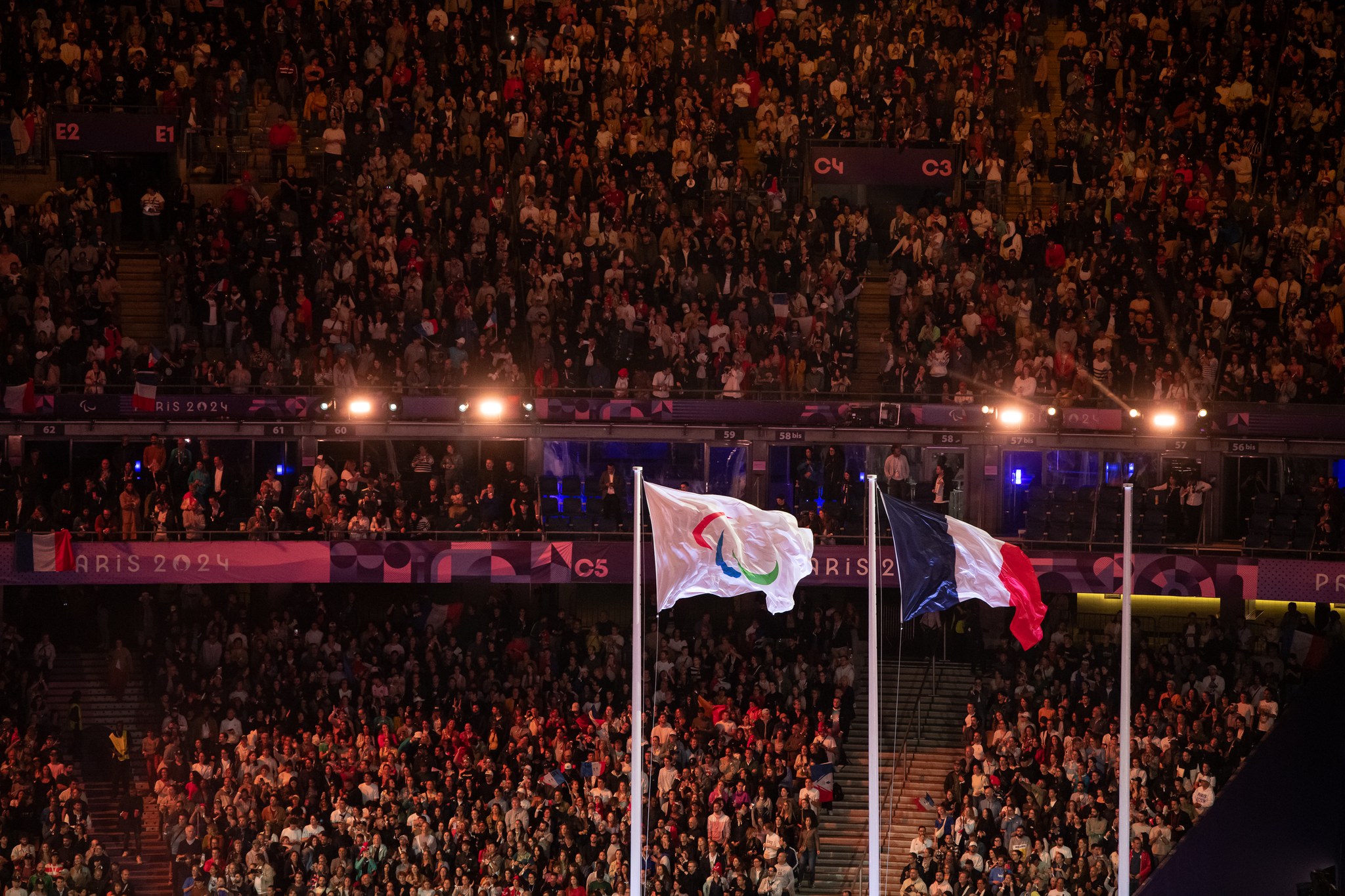 Kuva Pariisin 2024 paralympialaisten päättäjäisistä. Suuri yleisö katsomossa ja heidän edessään liehuu IPC:n ja Ranskan lippu.