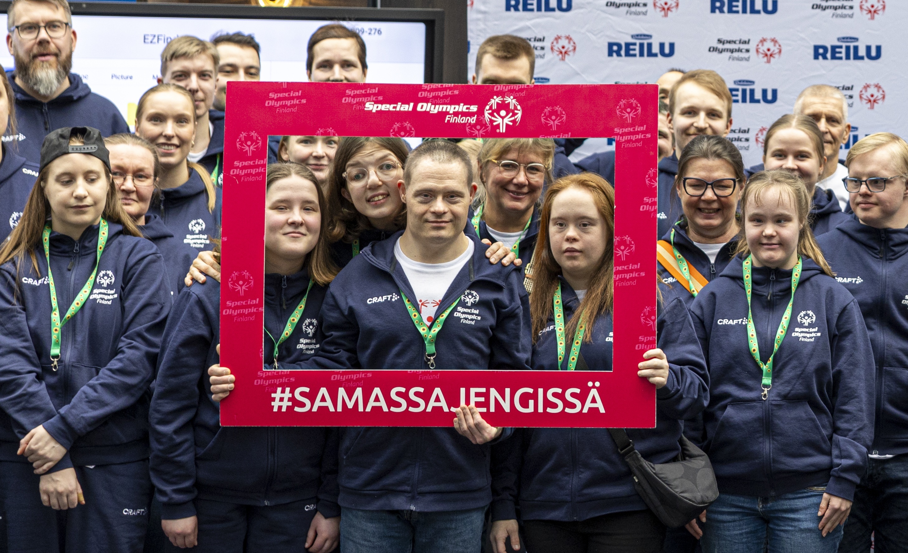 Iloiset SO-urheilijat hymyilemässä kameralle punaisen #SamassaJengissä -kehyksen sisällä.